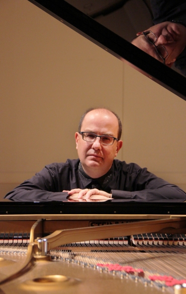 O rosto de Alexandre Dossin aparece entre a tampa e a parte interna de um piano, que funcionam como uma esp&eacute;cie de moldura na foto