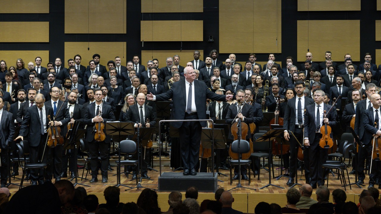 Maestro Manfredo Schmiedt agradece ao p&uacute;blico em frente a orquestra e ao coro sinf&ocirc;nico da OSPA 
